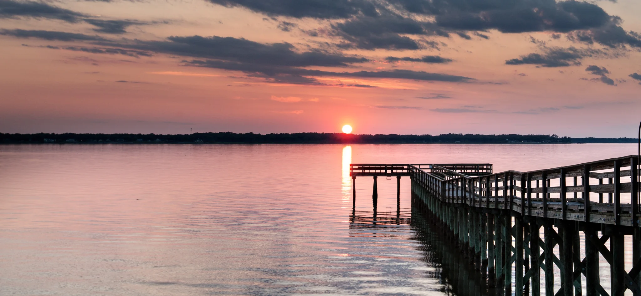 Sunset over the river, with a long wooden pier reaching out over the water