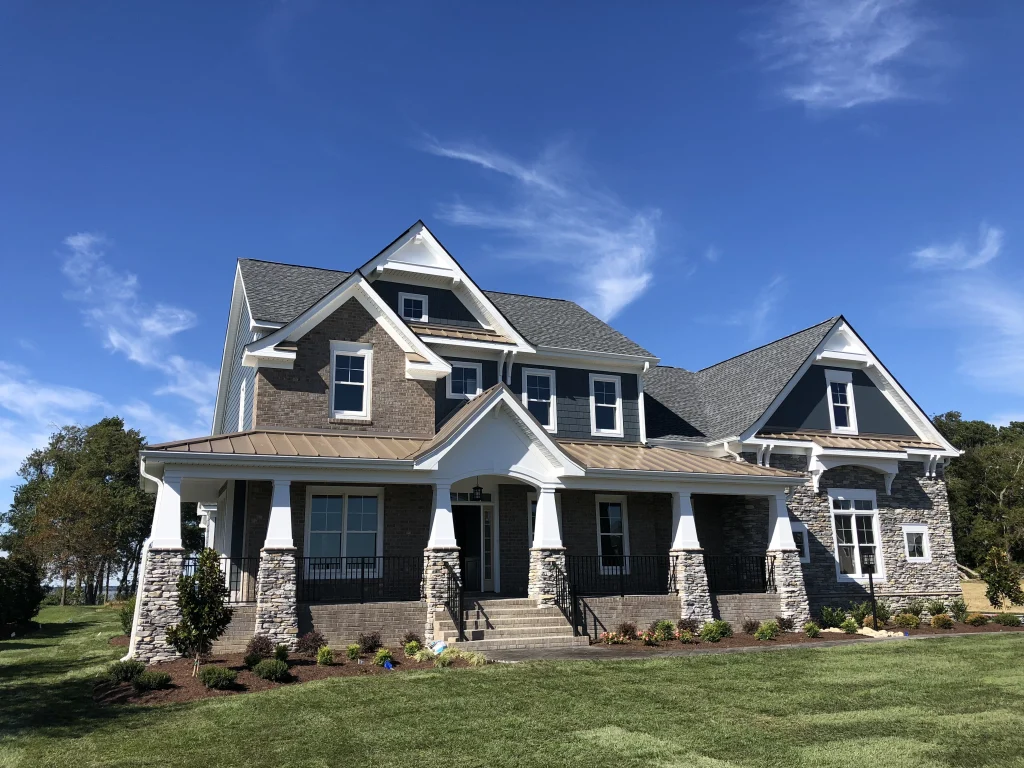Two-story custom home with gray shingle siding, white trim and stone porch columns under a deep blue sky